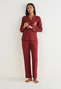 Rød ternet pyjamas sæt lavet af blødt stof, med lange ærmer, knaplukning og en bjørn broderi detalje på brystlommen.