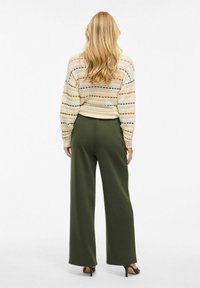 Krämfärgad stickad tröja med mönster och olivgröna vida byxor. Outfiten har en avslappnad passform och är matchad med svarta klackskor.
