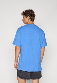 Blå bomulds t-shirt med korte ærmer, rund halsudskæring og en afslappet pasform. Stoffet har en let slidt tekstur, som er parret med mørke shorts.