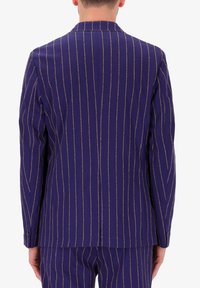 Blazer navy con righe verticali dorate. Presenta un colletto a punta, polsini con bottoni e una texture liscia. Vestibilità su misura e dettagli minimi.