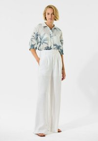 Lichte, gestreepte blouse in blauw en wit, met een kraag en korte, gathered mouwen; gecombineerd met hoog-wijde witte pantalons.