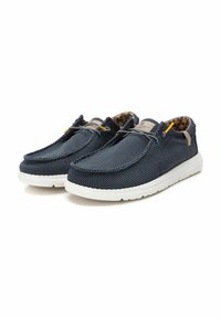 Zapatillas slip-on de lienzo azul marino con un exterior texturizado, suela de goma blanca y acentos amarillos y azules. Forradas con un interior estampado.
