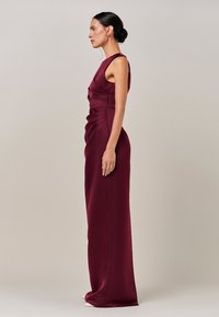 Vínové šaty bez rukávů se zdobením s řasením, přiléhavým živůtkem a dlouhou sukní s hladkou texturou.