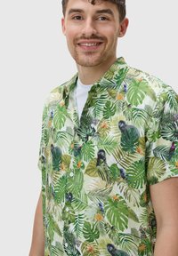 Camicetta a maniche corte in tessuto verde chiaro con stampa di foglie tropicali e animali, dotata di colletto alla camicia e bottoni bianchi.