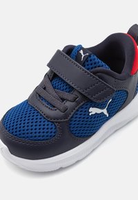 Chaussure de sport bleue et grise en matériaux en maille et cuir, avec sangle Velcro et semelle blanche ; présente le logo Puma en blanc.