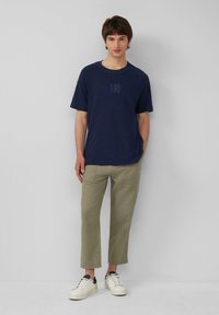 Marineblaue kurzärmelige T-Shirt mit strukturiertem Muster auf der Vorderseite; kombiniert mit hellgrünen Hosen und weißen Sneakers mit schwarzen Akzenten.