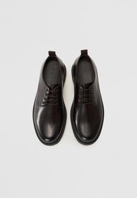 Zwarte leren schoenen met een gladde afwerking, ronde neus en vetersluiting. Beschikt over een gestructureerde zwarte rubberen zool en een kleine hak.