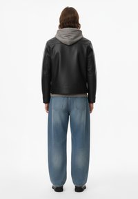 Giacca di pelle nera con felpa con cappuccio grigia sotto, abbinata a jeans a gamba larga azzurri. Texture liscia, design casual e moderno.
