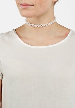 Collier ras du cou en perles de cristal clair, doté d'un design à double brin, porté autour du cou sur un fond pâle, associé à une chemise blanche.