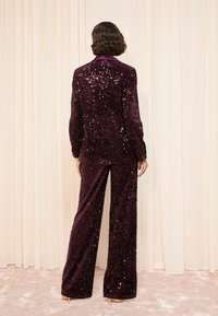 Burgundy sequin jacket and matching pants, with a smooth texture and wide legs, featuring a notched collar and long sleeves.