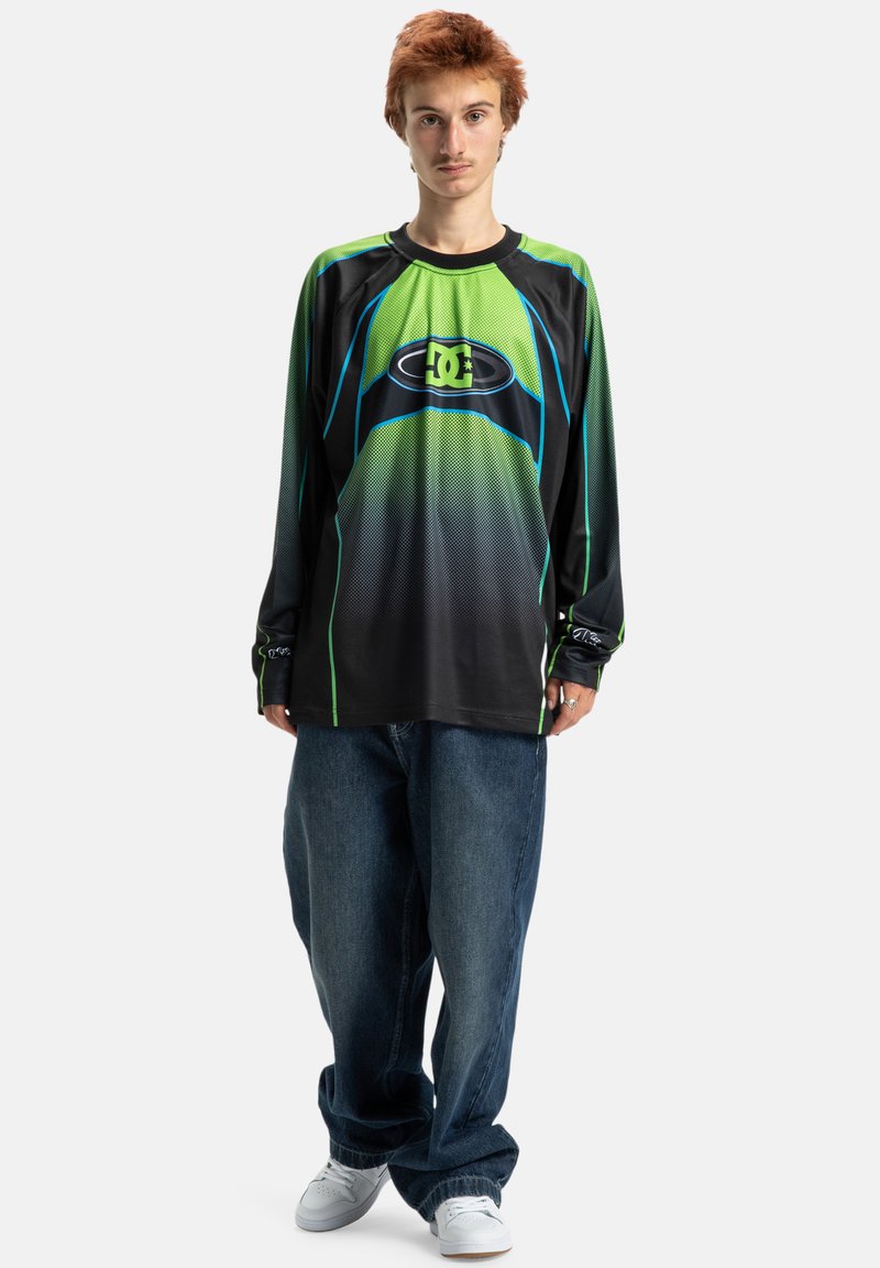 Tricou negru cu mânecă lungă, cu un design în gradient verde și albastru, având un logo mare și un textura de plasă. Purtați cu blugi albastri cropped.