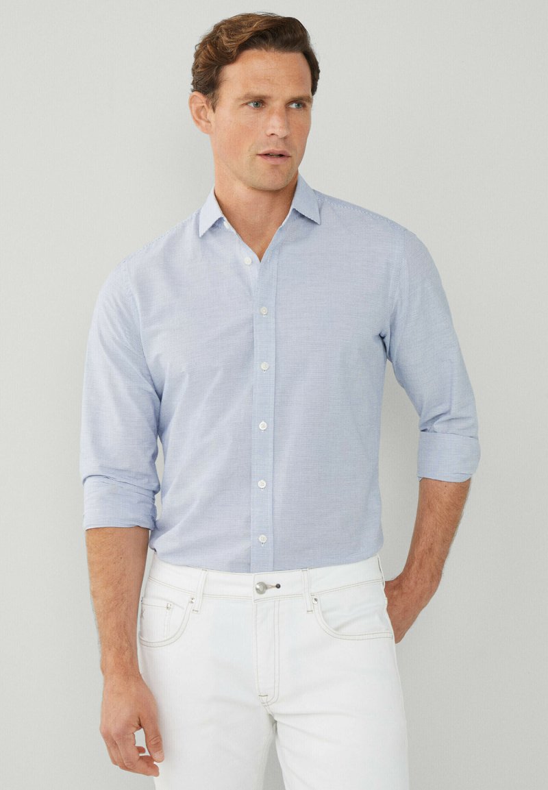 Camicia a righe azzurro chiaro con colletto button-down, maniche arrotolate e bottoni bianchi, abbinata a pantaloni bianchi. Tessuto dalla texture liscia.