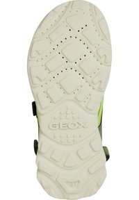 Bílé gumové podrážky s texturovaným vzorem, s logem "GEOX". Zelené akcenty na boku, navržené pro prodyšnost s více otvory.