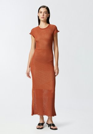 Vestido de punto en color óxido con mangas cortas, patrones texturizados y aberturas laterales. Combinado con sandalias negras de tacón.