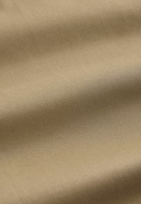 Tissu beige lisse avec une fine texture côtelée diagonale et des plis doux créant de légères ombres.