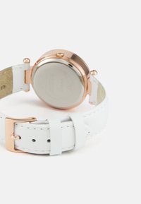 Ring käekell roosa kuldse korpuse, valge nahkrihma ja kinniseguga, vaadatuna tagantpoolt valgel taustal.