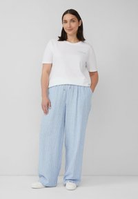 Witte katoenen t-shirt met blauwe geborduurde tekst, gecombineerd met lichtblauwe gestreepte, ruime pyjamabroek en witte instapschoenen.