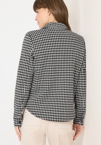 Czarna i biała, w kratkę, długa koszula z długim rękawem, z kołnierzykiem, zapinanymi mankietami i zaokrąglonym dołem, wykonana z lekkiego materiału.