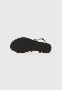 Sandalha plana preta com uma sola de borracha suave, tiras finas e uma fivela dourada. Projetada para um ajuste de dedo do pé aberto.