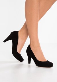 Chaussures à talons hauts en daim noir avec un bout arrondi et une finition lisse. Le talon mesure environ 10 cm de haut et a une texture douce.
