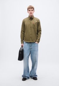 Πουκάμισο χακί με κουμπιά και τσέπη στο στήθος, σε συνδυασμό με ανοιχτό μπλε φαρδιά τζιν παντελόνια. Μαύρη τσάντα και μαύρα παπούτσια.