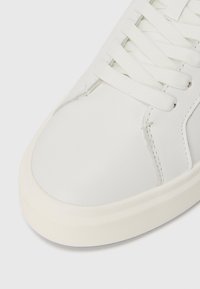 Sneaker din piele albă cu șireți albi plat, suprafață netedă, vârf rotunjit, design minimalist și accente subtile de cusături pe lateral.