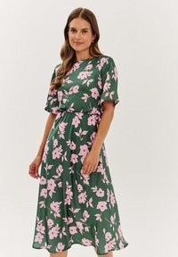 Kvetinové šaty zo zelenej tkaniny s ružovými kvetmi. Krátke rukávy a stiahnutý pás. Plynulý dizajn, po kolená s jemnou textúrou.