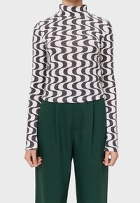 Langärmliges Oberteil mit hohem Kragen, gestaltet mit einem schwarz-weißen Wellenmuster, aus strukturiertem Stoff und kombiniert mit high-waisted grünen Hosen.