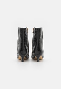 Bottines noires avec texture crocodile, talon slim et zips dorés à l'arrière. Fini lisse et design à bout pointu.
