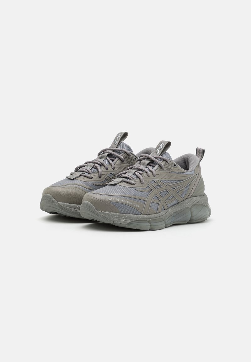 Graue Sportschuhe mit strukturiertem Mesh-Obermaterial und gepolsteter Sohle. Merkmale umfassen Schnürsenkel, eine Markierung auf der Zunge und Gummielemente an der Sohle.