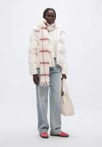 Λευκό μπουφάν puffer, ανοιχτό γκρι πουλόβερ, καρό κασκόλ σε ροζ και κρέ μ, μπλε τζιν με φαρδιά μπατζάκια, ροζ παπούτσια και λευκή τσάντα tote.