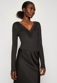 Must black bodysuit pikema varrukatega, sügava V-kaelusega, pitsist äärisega; sile tekstuur ja keha lähedane disain, koos satiinist seeliku pari.