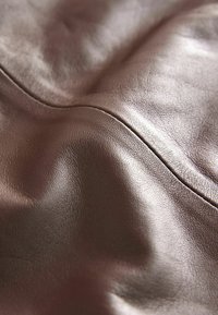Gros plan sur un cuir marron montrant une texture lisse avec un léger éclat, présentant des coutures cousues et des plis délicats.