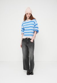 Πουλόβερ με ρίγες σε μπλε και ροζ, συνδυασμένο με μαύρο τζιν με κοφτά μπατζάκια. Το πουλόβερ διαθέτει απαλή, υφή με ανάγλυφη επιφάνεια, ενώ το σύνολο ολοκληρώνεται με μαύρα παπούτσια.