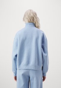 Hellblauer Sweatshirt mit hohem Kragen, lockerer Passform, gerippten Bündchen und Saum. Weicher, strukturiert aussehender Stoff auf der Rückseite.