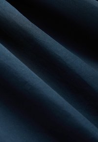 Tissu bleu foncé à texture fine, présenté en plis doux créant des ombres et des reflets subtils.