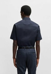 Camicetta corta navy con colletto a punta, abbinata a pantaloni a quadri. Tessuto liscio con vestibilità sartoriale e silhouette strutturata.