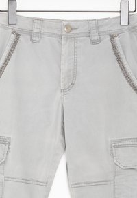 Ljusgrå byxor med framknapp, bälteshällor, metallbeslagna diagonala fickkantar och en ficka med lock på höger lår.