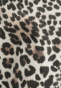 Tissu beige avec vue rapprochée d'un motif léopard irrégulier noir et marron sur une surface textile texturée.
