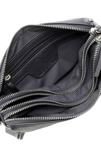 Interno di una borsa in pelle nera con molteplici scomparti con zip, caratterizzato da una texture liscia e dettagli in cerniera argentata. Foderato con tessuto scuro.