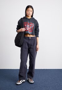Cropped, black hoodie with red and white graphic, paired with loose, navy pants and black and white sneakers. Accessory: quilted shoulder bag.