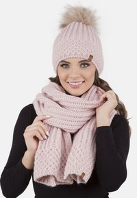 Căciulă tricotată roz cu un pompon din blană și fular texturat asortat, având accente modelate și o textură moale, groasă.