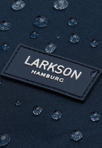 Tengerészkék anyag vízcseppekkel, fekete, téglalap alakú címkével, melyen fehér betűkkel szerepel a "LARKSON HAMBURG" felirat.