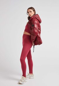 Röd puffjacka med huva, kombinerad med en matchande ribbad topp och leggings. Silverfärgade sneakers med snörning. Slät textur, strukturerad passform.