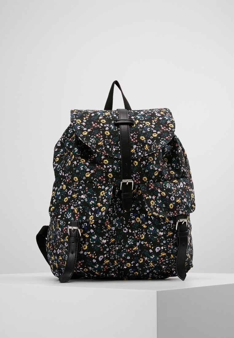 Sac à dos noir à motif floral avec rabat pliant, bretelles réglables et accents en cuir. Comprend plusieurs poches et un tissu texturé.