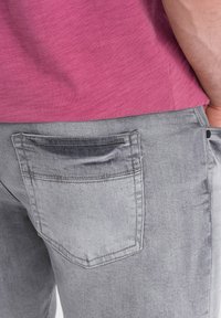Vaqueros de mezclilla gris con una textura desteñida y un bolsillo trasero. Los vaqueros se combinan con una camiseta rosa de textura.