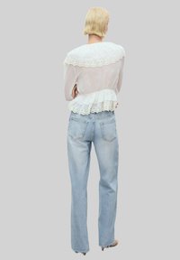 Vit blus med spetsdetaljer och volangkanter, matchad med ljusblå mom-jeans med hög midja. Slät textur, avslappnad passform och minimal detaljering.