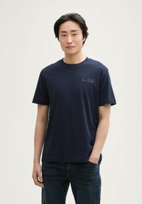 Tricou din bumbac bleu marin, cu mâneci scurte, gât rotund și logo subtil pe piept. Textură moale și croială lejeră.
