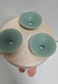 Houten basis met drie lichtgroene siliconen zuignappen en een zilveren schroef in het midden; logo en certificeringsmarkeringen zichtbaar.