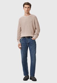 Jasno beżowy sweter dzianinowy, niebieskie dżinsy, czarny pasek i ciemne buty. Sweter ma prążkowaną fakturę i klasyczny okrągły dekolt.